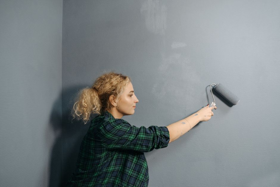 Artisan appliquant au rouleau une peinture grise sur un mur intérieur